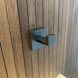 Een gunmetal handdoekhaak met een vierkante rozet, is gemonteerd op een verticaal houten paneel.