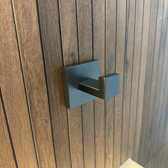 Een gunmetal handdoekhaak met een vierkante rozet, is gemonteerd op een verticaal houten paneel.