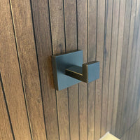 Een gunmetal handdoekhaak met een vierkante rozet, is gemonteerd op een verticaal houten paneel.