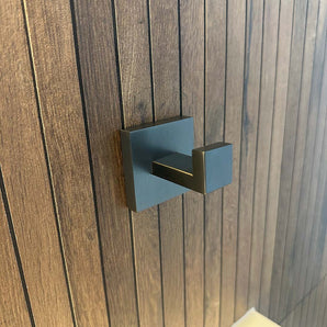 Een gunmetal handdoekhaak met een vierkante rozet, is gemonteerd op een verticaal houten paneel.