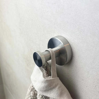 Een Midao RVS WC-set wandhaak van yessential.nl houdt een beige handdoek met een lus en textuur tegen een gladde, lichtgekleurde muur.