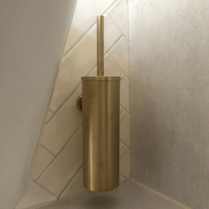 De Romano Gold WC-set van yessential.nl, met een gouden afwerking en een bijpassende cilindrische houder, is aan de muur bevestigd op witte diagonale tegels en voegt een vleugje elegantie toe aan je badkameraccessoires.