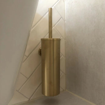 De Armando Gold Set van yessential.nl bestaat uit een gouden toiletborstel met bijpassende cilindervormige houder. Gemonteerd in de hoek, steekt hij af tegen diagonaal gerangschikte witte wandtegels voor een elegante look.