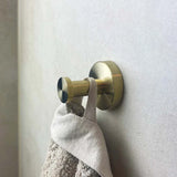 De Kyano Gold Hook van yessential.nl houdt een handdoek met beige textuur vast in een moderne, minimalistische badkamer met een lichtgrijze muur.