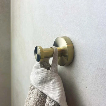 De Kyano Gold Hook van yessential.nl houdt een handdoek met beige textuur vast in een moderne, minimalistische badkamer met een lichtgrijze muur.