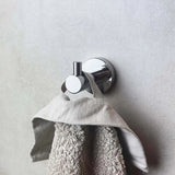 Een Quirino Chromen WC-set van yessential.nl houdt een handdoek met grijze textuur aan zijn ophanglus tegen een gladde, lichtgekleurde muur.
