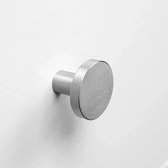 Een ronde, geborsteld metalen wandhaak uit de Marizo RVS lijn van yessential.nl is gemonteerd op een wit oppervlak. Hij heeft een minimalistisch ontwerp met een cilindrische basis en een plat rond gezicht, vergelijkbaar met de Marizo Deluxe meubelknoppen.