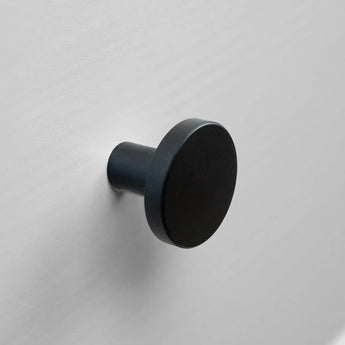 De Marizo Black van yessential.nl is een ronde zwarte wandhaak met een matte afwerking, gemonteerd op een lichtgrijze muur. Het minimale ontwerp en het platte ronde gezicht maken het ideaal als meubelknopjes zwart voor moderne interieurs.