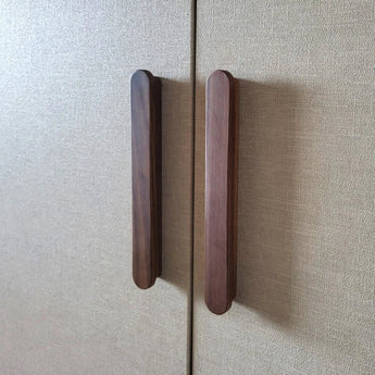 Twee Arriero Walnut handgrepen van yessential.nl zijn bevestigd aan de deuren van een kast met beige structuur, dicht bij elkaar geplaatst langs de naad waar de twee deuren elkaar raken.