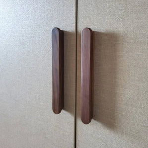 Twee Arriero Walnut handgrepen van yessential.nl zijn bevestigd aan de deuren van een kast met beige structuur, dicht bij elkaar geplaatst langs de naad waar de twee deuren elkaar raken.