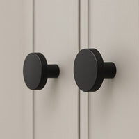 Twee Marizo Black meubelknopjes van yessential.nl met een matte afwerking zijn gemonteerd op een lichte, verticaal gegroefde kast. Hun minimalistische ontwerp contrasteert prachtig met de neutrale achtergrond.