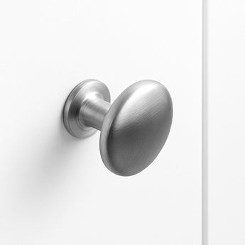 De Pedro RVS deurknop van yessential.nl heeft een geborsteld metalen ovaal ontwerp, gemonteerd op een effen witte deur en in close-up getoond met een minimalistische stijl en zachte verlichting.