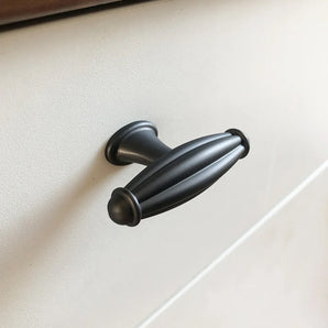 Een close-up van de Alvaro Antraciet knop van yessential.nl, met een donker metalen, ovaalvormig, geribbeld ontwerp op een wit kast- of ladefront.