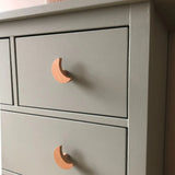 Close-up van de Bambino Moon commode van yessential.nl, met lichtgrijze lades met houten maanvormige knoppen. Met zijn gladde matte afwerking en moderne ontwerp is het een stijlvolle keuze voor elke kinderkamer.