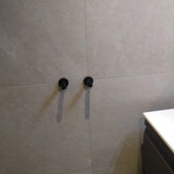 Twee Justo Black Hooks van yessential.nl zijn gemonteerd op een beige betegelde muur en werpen oogschaduwen. Een wit aanrechtblad en een donkere kast verschijnen gedeeltelijk aan de rechterkant.
