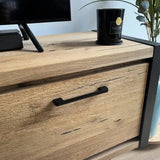 Een close-up van de Ramiro Black Deluxe kast van yessential.nl, met luxe handgrepen, een tv-standaard, een zwarte kaars met het label Black Oud en een deel van een groene plant op de achtergrond.