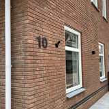 Een bakstenen gebouw met een raam en deur, met naast de ingang het strakke yessential.nl Adamo Black 20cm huisnummer.
