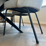 Close-up van moderne stoelen met lichte kussens en zwarte metalen poten, voorzien van yessential.nl's Paco Set Ø 21-25mm stoelpoten beschermers voor vloerbescherming, op een houten vloer in een lichte, minimalistische kamer.