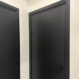 Twee Ludo Black 89x89 deuren van yessential.nl, met een matzwarte afwerking, eenvoudige handgrepen en zwarte scharnieren, zijn geplaatst in witte hoekwanden voor een strakke, moderne look.