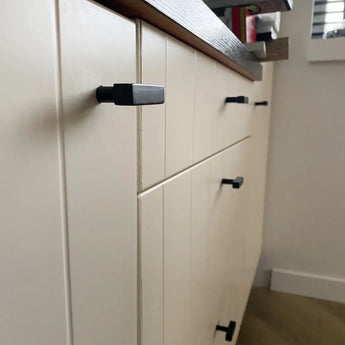 Close-up van crèmekleurige kastladen met de Vigio Black Knob van yessential.nl, naast een bruin houten aanrechtblad in een lichte kamer met lichte vloeren.