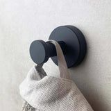 De Kyano Black Hook van yessential.nl heeft een rond, matzwart ontwerp dat een beige stoffen lus vasthoudt tegen een lichte muur - een ideale moderne touch voor elke badkamer.