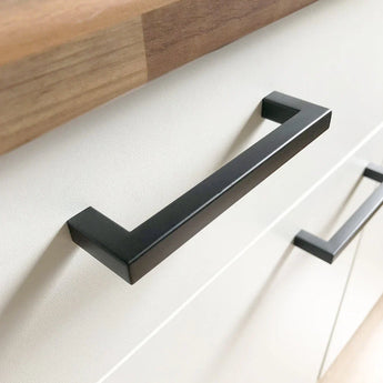 Een close-up van de Vasco Black keukenhandgreep van yessential.nl op een witte kast met een houten aanrechtblad. Op de achtergrond is een andere Vasco Black keuken handgreep zichtbaar.