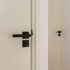 Een close-up van de Domaso Black deurklinken en slot van yessential.nl op een witte deur, met op de achtergrond een tweede deur voorzien van vergelijkbare vierkante zwarte deurklinken.