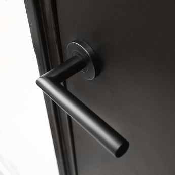 Een close-up van de Lucio Black deurklink van yessential.nl, met een matzwarte cilindrische greep horizontaal gemonteerd op een donkere deur - een strak voorbeeld van moderne zwarte deurklinken.
