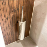 De Xavo Chroom WC-set van yessential.nl - een slanke zilverkleurige toiletborstelhouder met deksel - steekt af tegen verticale houten panelen en lichte tegels in een moderne badkamer.