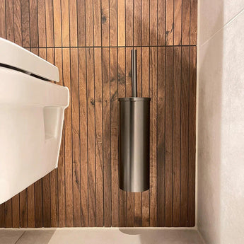 Een moderne badkamer is voorzien van een wit toilet en de Armando Gunmetal Set van yessential.nl, gemonteerd op een verticale houten paneelwand. Lichtgekleurde tegels versterken de luxe uitstraling van deze badkameraccessoires.