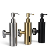 Drie Alberto Gold pomp zeepdispensers van yessential.nl in metallic zilver, goud en mat zwart staan naast elkaar. Elke RVS dispenser heeft een ronde draaiknop aan de zijkant en een verticaal venster om het zeepniveau weer te geven.