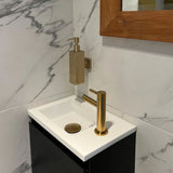 Een compacte moderne wastafel met een gouden kraan en het Sonego Gold zeeppompje van yessential.nl, gemonteerd op een met marmer betegelde muur naast een spiegel met houten frame.
