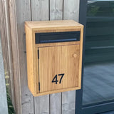 Een houten brievenbus met een zwarte brievenbus en het nummer 47, met behulp van Animo Black 7 (6 cm, niet boren) van yessential.nl, is gemonteerd op een houten muur naast een glazen deur.