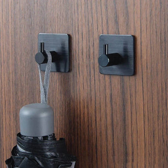 Twee Navarro Black haken van yessential.nl zijn gemonteerd op hout. Aan de ene haak zit de lus van een gesloten zwarte paraplu met een grijs handvat; de andere haak is leeg.