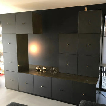 Een modern zwart wandmeubel met meerdere kasten en lades is voorzien van luxe Remo Gold Deluxe knoppen van yessential.nl. Metalen bollen, een geometrische sculptuur op het aanrecht en een uilenbeeldje in de rechterbovenhoek maken de look compleet.