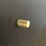 Een enkele Remo Gold Deluxe knop van yessential.nl, met een cilindrisch gestructureerd ontwerp, is gemonteerd op een glad donkergrijs oppervlak.