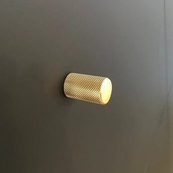 Een enkele Remo Gold Deluxe knop van yessential.nl, met een cilindrisch gestructureerd ontwerp, is gemonteerd op een glad donkergrijs oppervlak.