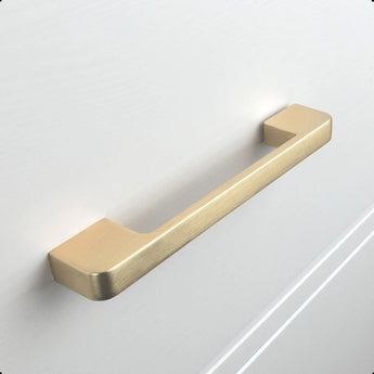 Een Ramiro Gold Deluxe keukenkast greep van yessential.nl, met een mat gouden afwerking, is gemonteerd op een witte kastlade met een glad oppervlak en subtiele groeven.
