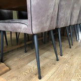 Een close-up van moderne eetkamerstoelen met zwarte metalen poten beschermd door yessential.nl Paco Set Ø 21-25mm siliconen stoelpoten beschermers en lichtgrijze zittingen, gerangschikt rond een houten eettafel op een lichtbruine houten vloer.