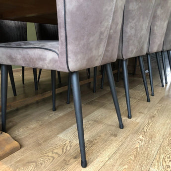 Een rij zacht grijsbruin gestoffeerde eetkamerstoelen met zwart metalen poten, elk voorzien van yessential.nl's Paco Set Ø 25-29mm anti-kras vilt stoelpootdoppen, omringt een houten tafel op een lichtbruine houten vloer.