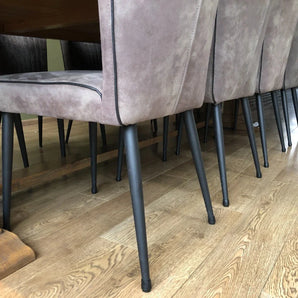 Een close-up van moderne eetkamerstoelen met lichtgrijze zittingen en zwarte metalen poten voorzien van yessential.nl Paco Set Ø 12-16mm, gerangschikt rond een houten eettafel op een lichtbruine houten vloer.