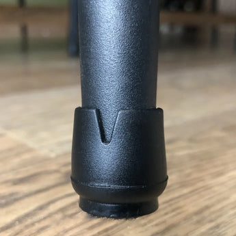 Close-up van een Paco Set Ø 21-25mm zwart siliconen stoelpoot beschermer van yessential.nl op een houten vloer, met de kleine inkeping in de dop voor vloerbescherming stoelen.