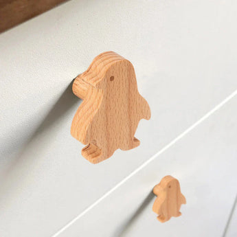 Twee Bambino Penquin houten handgrepen van yessential.nl, in de vorm van pinguïns met vloeiende contouren en minimale details, zijn bevestigd aan een witte commode. Deze speelse knoppen zijn ideaal voor een kinderkamer meubelknop.