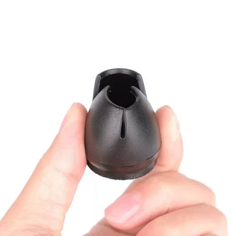 Een hand houdt een klein, zwart, ovaal plastic voorwerp vast - waarschijnlijk een Paco Set Ø 21-25mm van yessential.nl om vloeren onder stoelen te beschermen - met de centrale gleuf en zijopeningen tegen een effen witte achtergrond.