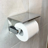 Een rol toiletpapier is gemonteerd op een Tazio Chrome (No Drill) houder van yessential.nl, met een plat, rechthoekig deksel in een betegelde badkamer.