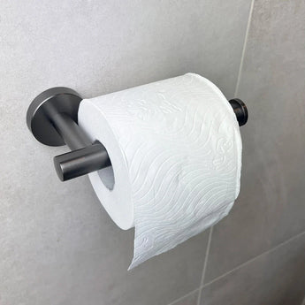 Een rol wit toiletpapier met een subtiel reliëfpatroon hangt aan de Lorenzo Gunmetal WC-set van yessential.nl, gemonteerd op een lichtgekleurde betegelde badkamermuur.