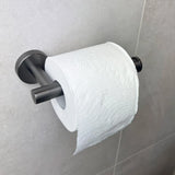 Een rol wit toiletpapier hangt aan de Corrado Gunmetal WC-set van yessential.nl, een luxe collectie toiletaccessoires, gemonteerd op een lichtgrijs betegelde badkamermuur.