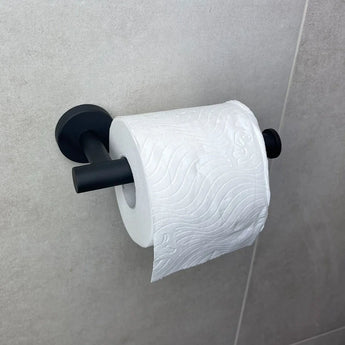 De Cosimo Black WC-set van yessential.nl heeft een rol toiletpapier op een matzwarte wandhouder, afgebeeld tegen lichtgrijze badkamertegels. Het toiletpapier met subtiel reliëf voegt elegantie toe aan je badkameraccessoires.