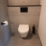 Een moderne badkamer met het yessential.nl Vero Black Deluxe wandcloset, luxe toiletaccessoires, een zwart spoelpaneel boven, zwarte toiletborstelhouder rechts, vierkante toiletrolhouder links en grijs betegelde muren en vloer.