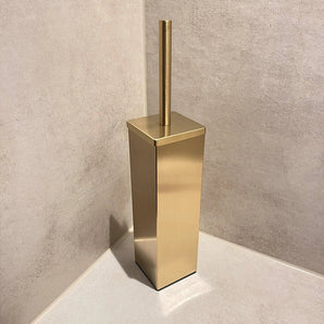 De Velasco Gold toiletborstel van yessential.nl, vrijstaand met houder, staat in de hoek van een badkamer met beige betegelde muren en vloer.